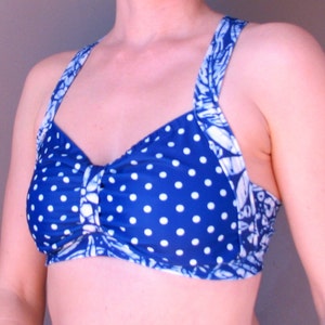 Puede incluir: Un top de bikini azul y blanco con lunares y una tira con estampado floral. El top tiene un detalle fruncido en el centro.