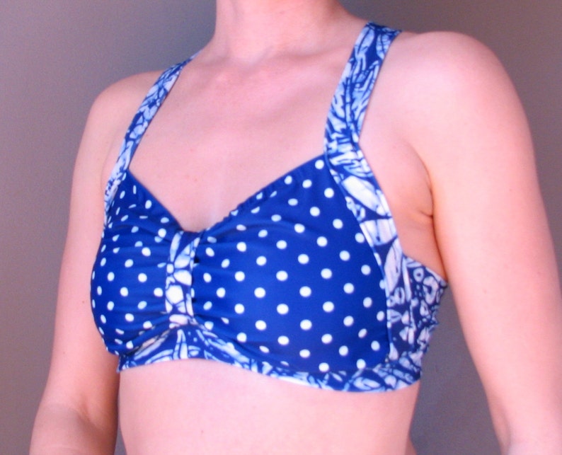 Puede incluir: Un top de bikini azul y blanco con lunares y una tira con estampado floral. El top tiene un detalle fruncido en el centro.