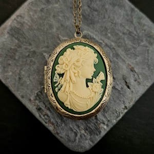 Könnte beinhalten: Eine goldene Halskette mit einem grünen Kamee, das das Profil einer Frau mit einer Blume im Haar zeigt.