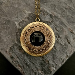 May include: A gold pendant necklace with a round, ornate design. The pendant features a black gemstone in the center.