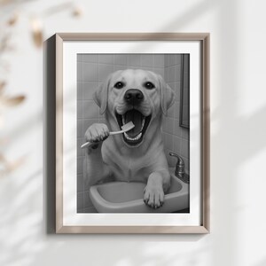 May include: Black and white framed print of a yellow Labrador Retriever dog brushing its teeth in a bathroom sink. The dog has its mouth open wide, holding a toothbrush. The image is in a bathroom setting.