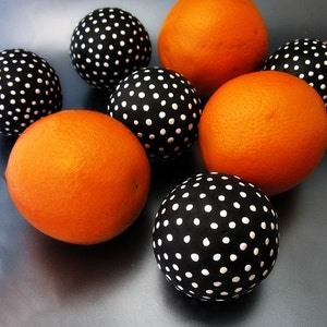 Puede incluir: Arreglo de naranjas y esferas negras con lunares blancos. Las naranjas son de color naranja brillante y tienen una superficie texturizada. Las esferas negras están salpicadas de puntos blancos, creando un patrón contrastante.