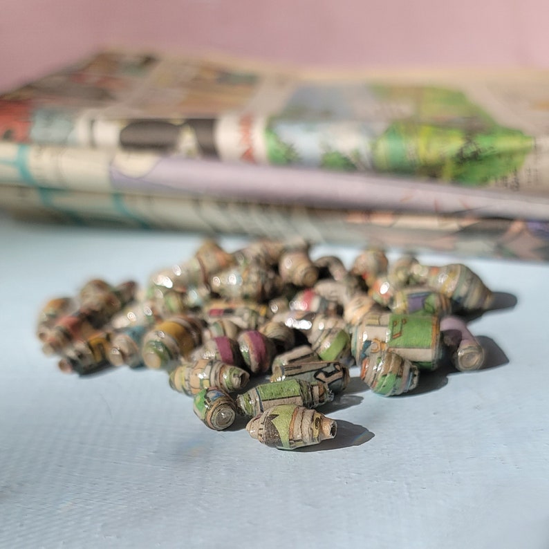 May include: A close-up of a pile of colorful paper beads. The beads are made from rolled up pieces of paper and have a variety of patterns and colors.