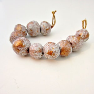 May include: A necklace of large, round beads. The beads are a metallic copper colour with a distressed white finish. The beads are strung on a thin, brown cord, forming a circular shape.