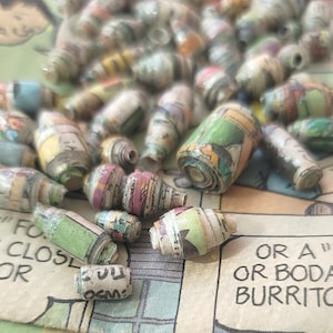 May include: A close-up of a collection of colorful paper beads made from recycled comic books. The beads are rolled and have a variety of patterns and colors.