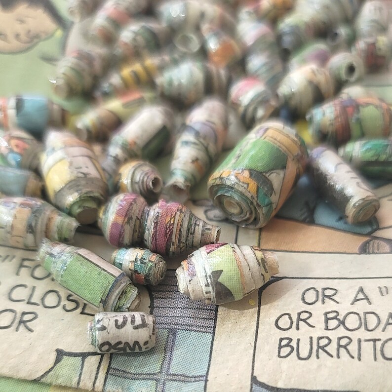 May include: A close-up of a collection of colorful paper beads made from recycled comic books. The beads are rolled and have a variety of patterns and colors.
