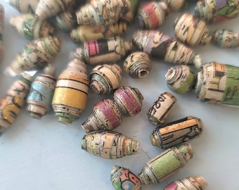 May include: A collection of colorful paper beads made from rolled up pages of comic books. The beads are various sizes and shapes, with some having a striped pattern.