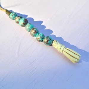 Peut inclure: Un collier de perles turquoise et or avec un pompon blanc. Les perles sont rondes et ont une finition vieillie.