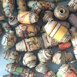 May include: A collection of colorful, handmade beads made from rolled up paper. The beads are various sizes and shapes, with some featuring patterns and text.
