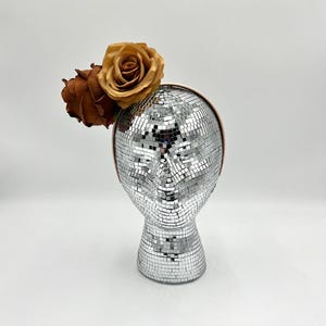 May include: A headband with two brown and gold fabric roses on a silver disco ball mannequin head.