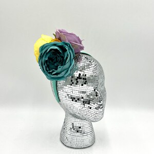 May include: A teal, yellow, and purple flower headband on a silver mannequin head.