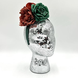 May include: A green and red fabric flower headband. The headband is on a silver mannequin head.