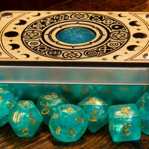 May include: A wooden box with a circular design and a blue iridescent lid, containing teal iridescent dice with gold numbers.