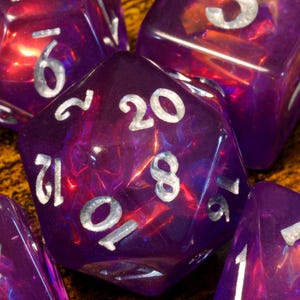 May include: A set of iridescent purple dice with silver numbers. The dice are a D20, D12, D10, D8, D6, and D4.