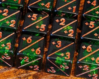 May include: Close-up of several square dice with a black and green marbled design. The numbers are in a copper color, and the dice have diagonal lines. The dice are arranged on a wooden surface.