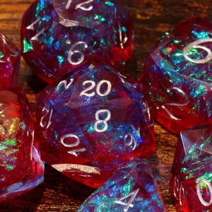 May include: A collection of polyhedral dice with a red and iridescent color scheme. The dice have white numbering and are designed for tabletop role-playing games. The dice are made of a clear resin with colorful inclusions.
