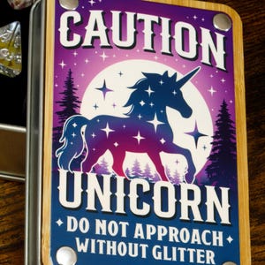 May include: A purple and blue wooden box with a metal lid. The box has a graphic of a unicorn with stars and a full moon. The text on the box reads "Caution Unicorn Do Not Approach Without Glitter".