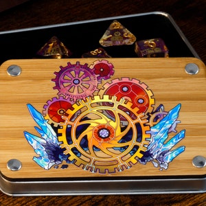 Può includere: Una scatola dadi in metallo con un coperchio in legno che presenta un design colorato di ingranaggi e cristalli intrecciati. Il coperchio ha un bordo in metallo argentato e quattro rivetti in metallo argentato.