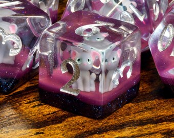 Juego de dados de gato gris: gato gris claro sobre una capa brillante de color morado oscuro y rosa.