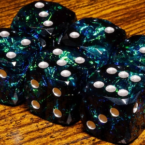 May include: A set of six translucent dice featuring a deep blue and emerald green iridescent foil interior. Each die has rounded edges and white circular pips indicating the numerical values on each of the six faces of the cube-shaped objects.