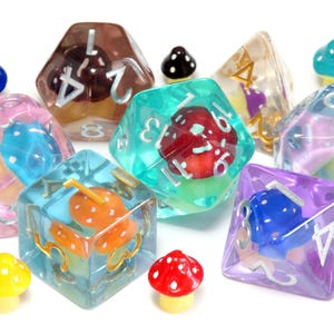 May include: A collection of translucent polyhedral dice featuring embedded miniature mushrooms in various colors, including red, orange, blue, and purple. The dice have silver or gold numbers, and several small, separate mushroom figurines are scattered around.