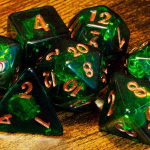 Peut inclure: Un ensemble de sept dés polyédriques vert émeraude translucides avec des chiffres de couleur cuivre. La collection comprend diverses formes telles qu'un d20, d12, d10, d8, d6 et d4, tous dotés d'arêtes vives et d'une finition polie avec des tourbillons internes.