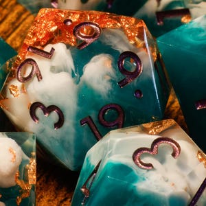 May include: Close-up of several polyhedral dice. The dice are teal and white with gold flecks and purple numbering. The dice are for tabletop games like Dungeons and Dragons.