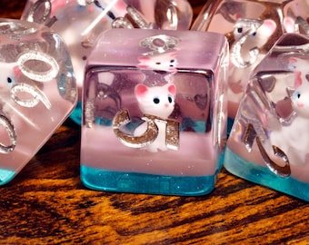 Juego de dados de gato blanco: dados poliédricos con un gato sobre una capa brillante de color rosa claro y azul.