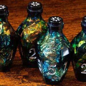 Peut inclure: Quatre bouteilles en verre irisé avec des bouchons noirs et des chiffres argentés. Les bouteilles ont un aspect unique, coloré et texturé, avec des nuances de bleu, de vert et d'or. Les bouteilles sont disposées sur une surface en bois.