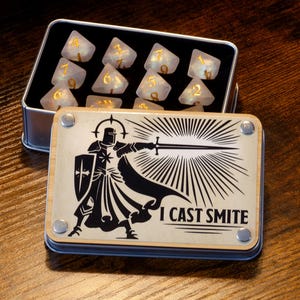 May include: A metal box with a black and white illustration of a knight holding a sword and the text "I cast smite". The box contains a set of white dice with gold numbers.