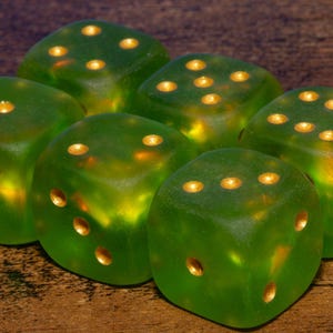 May include: A set of six translucent lime green dice with rounded corners and gold-colored pips. Each die features a smooth, frosted finish that allows light to pass through the material, highlighting the metallic gold indentations of the numbers.