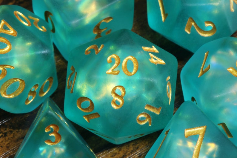 K&ouml;nnte beinhalten: Ein Satz tealblauer W&uuml;rfel mit goldenen Zahlen. Die W&uuml;rfel sind durchscheinend und haben eine schimmernde Oberfl&auml;che. Die Zahlen auf den W&uuml;rfeln sind 20, 8, 10, 16, 14, 7, 3, 2, 1, 5, 0 und 6.