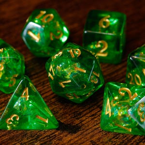Peut inclure: Un ensemble de sept dés polyédriques vert émeraude translucides avec des chiffres dorés. La collection comprend un d20, d12, d10, d8, d6 et d4, chacun présentant des bords nets et des chiffres clairs et lisibles gravés sur la résine verte.