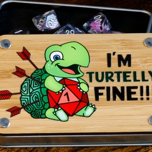 May include: A wooden box with a metal latch and a green turtle with arrows in its shell holding a red dice with a 1 on it. The box has a sign that says "I'm Turtlely Fine!!!"