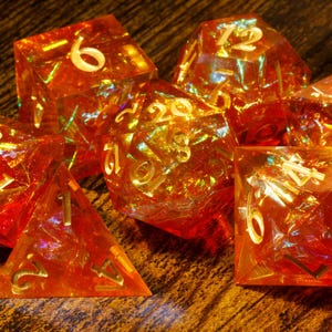 May include: A set of six iridescent orange dice with gold numbers. The dice are made of a clear material with a glittery finish.