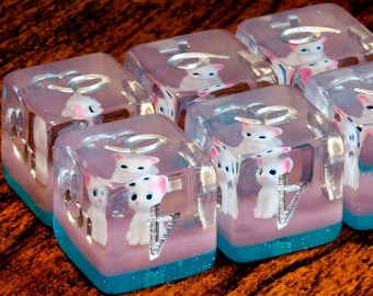 May include: A set of six translucent resin dice featuring embedded white cat figurines with pink ears. Each die has a pink base layer, a bright blue bottom section, and silver-coloured numerals. The dice are arranged in a cluster, showcasing the internal cat details and the reflective metallic numbers on the clear surfaces.