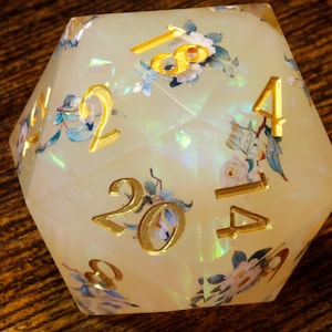 May include: A white iridescent d20 dice with gold numbers and floral designs. The numbers 1, 2, 4, 14, 20 are visible.