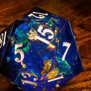 May include: A blue, iridescent, 20-sided die with gold flecks and white numbers. The die is showing the number 13.