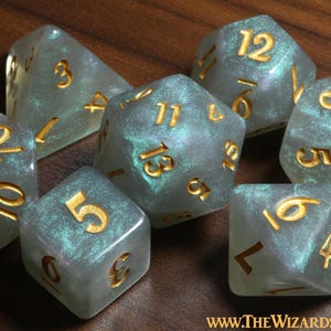 May include: Set of seven iridescent dice with gold numbers. The dice are a light blue colour with a pearlescent finish. The dice are in a variety of shapes, including a d4, d6, d8, d10, d%, d12, and d20.