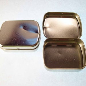 May include: Two silver metal rectangular tins with hinged lids. The tins are empty and have a shiny finish.