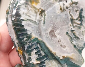 以下が含まれることがあります： 緑、白、茶色の瑪瑙でできた龍の彫刻で、中心に透明な水晶があります。龍は、細部までこだわってリアルなスタイルで彫られています。