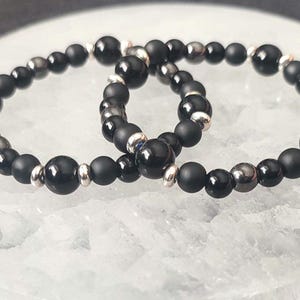 Puede incluir: Dos pulseras de cuentas negras con detalles plateados. Las pulseras est&aacute;n hechas de cuentas de &oacute;nix negro y hematites.