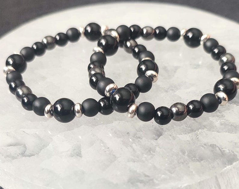 Puede incluir: Dos pulseras de cuentas negras con detalles plateados. Las pulseras est&aacute;n hechas de cuentas de &oacute;nix negro y hematites.