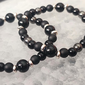 May include: Two black beaded bracelets with silver accents. The bracelets are made of black onyx and hematite beads.