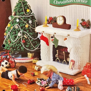 May include: A crocheted Christmas scene featuring a green tree, a white fireplace with stockings, and dolls playing with toys. The scene includes a red bicycle, a soccer ball, and wrapped gifts. The text "Christmas Corner" is visible.