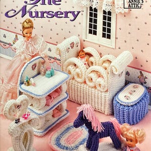 May include: A crochet pattern book cover titled "The Nursery" featuring a doll and various crochet dollhouse furniture. The furniture includes a crib, a changing table, a rocking horse, and a storage box. The color palette is primarily white, blue, and pink.