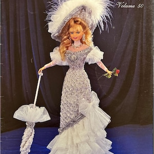 Puede incluir: Patrón de disfraz de coleccionista de crochet, volumen 50, para un vestido de cuentas, un sombrero y un paraguas. El patrón presenta una muñeca con un vestido plateado y blanco con un sombrero blanco y sosteniendo un paraguas blanco.