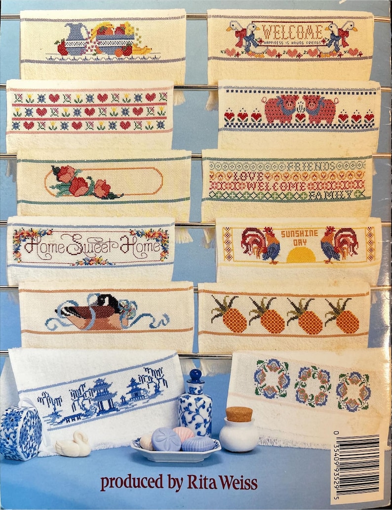 May include: A collection of embroidered decorative towels with various designs. Some towels feature floral patterns, while others display text like "Welcome" and "Home Sweet Home." The towels are displayed on a metal rack.