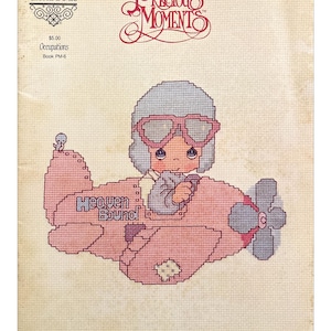 Puede incluir: Un patrón de punto de cruz con un personaje de Precious Moments en un avión rosa con las palabras "Heaven Bound". El diseño incluye una hélice, gafas de piloto y el texto "Designs by Gloria & Pat."