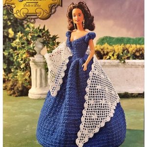 May include: A crochet doll wearing a blue dress and a white lace shawl. The doll is part of the "The Southern Belle Collection" and is named "Belle in Blue".